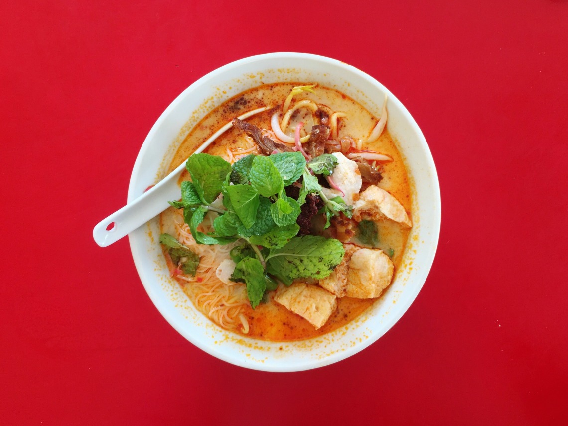 A bowl of curry mee on a red background